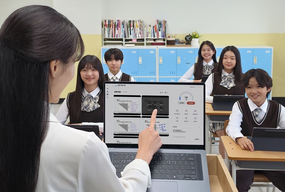 교사가 노트북에 띄운 녹스 클래스룸 화면에서 학생 태블릿 화면 하나를 가리키고, 뒤로 태블릿을 앞에 둔 학생들이 앉아 있는 교실 사진